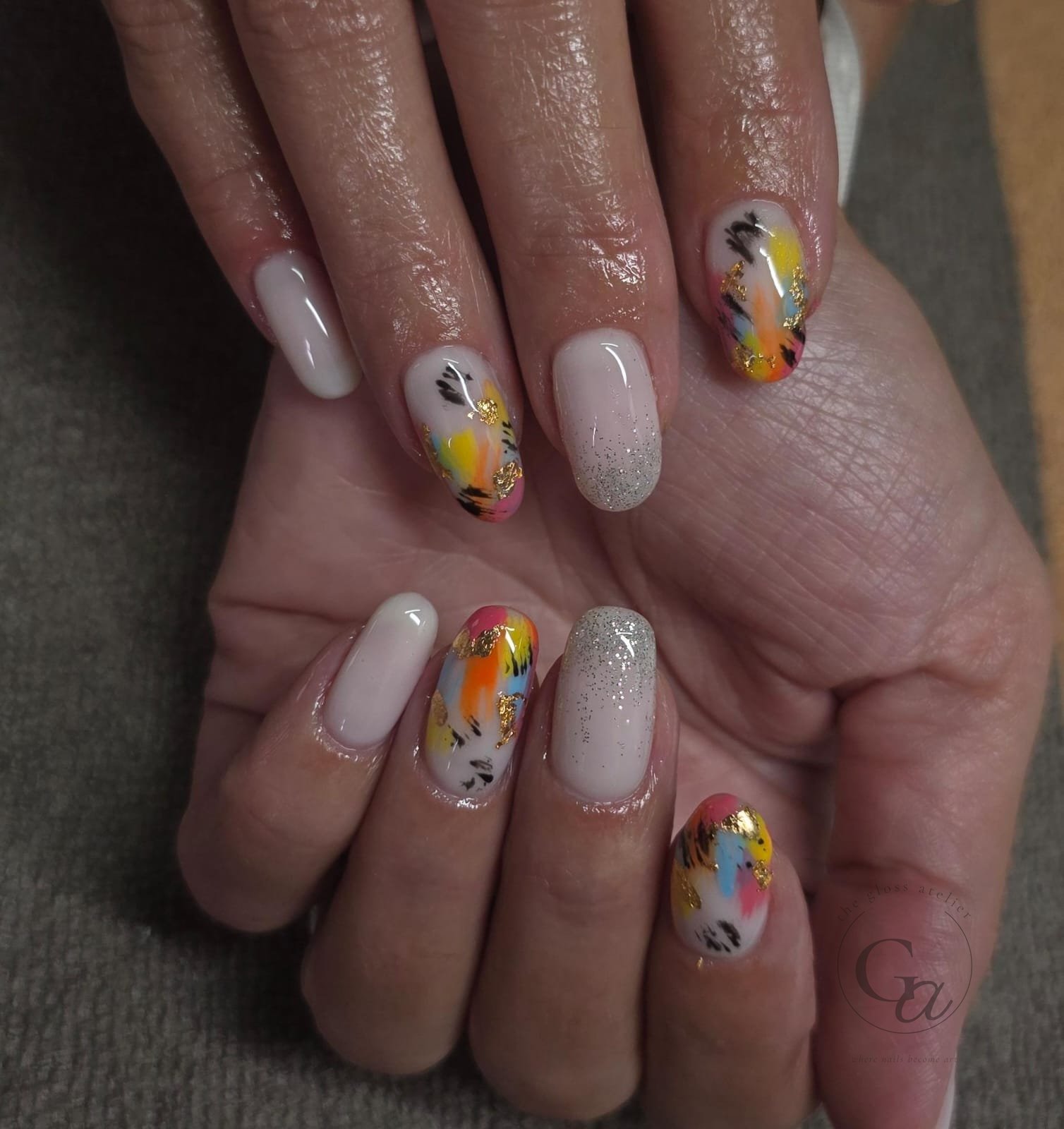 Milky white oval nails with abstract brushwork in yellow, blue and pink, gold leaf and silver glitter.