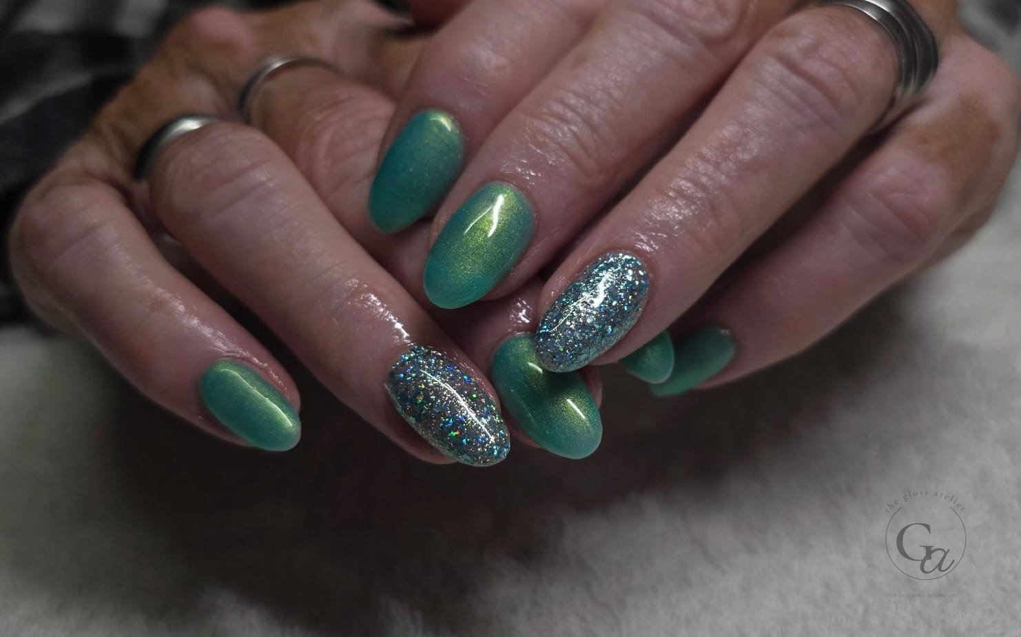 Teal cat-eye gel on almond nails with holographic glitter accents.