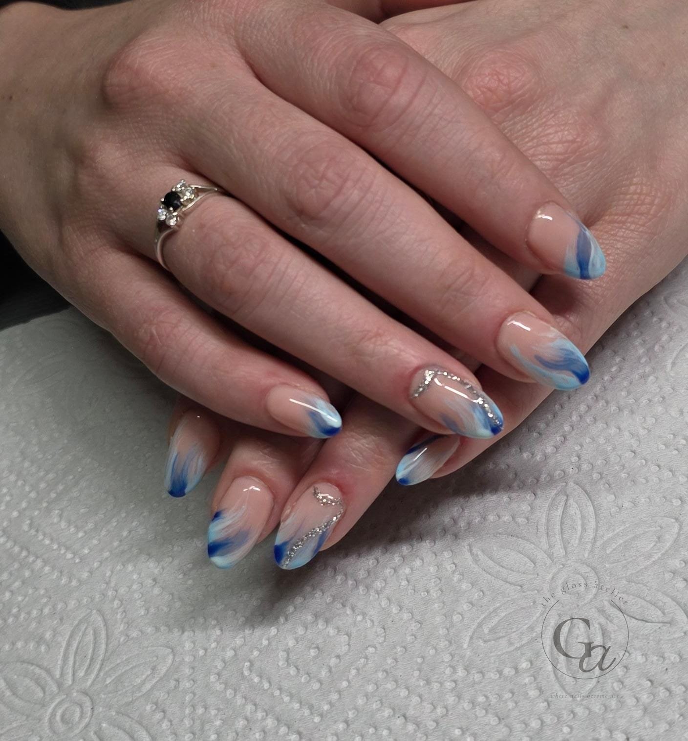 Blue and white marbled tips on almond nails with silver crystal swirls.
