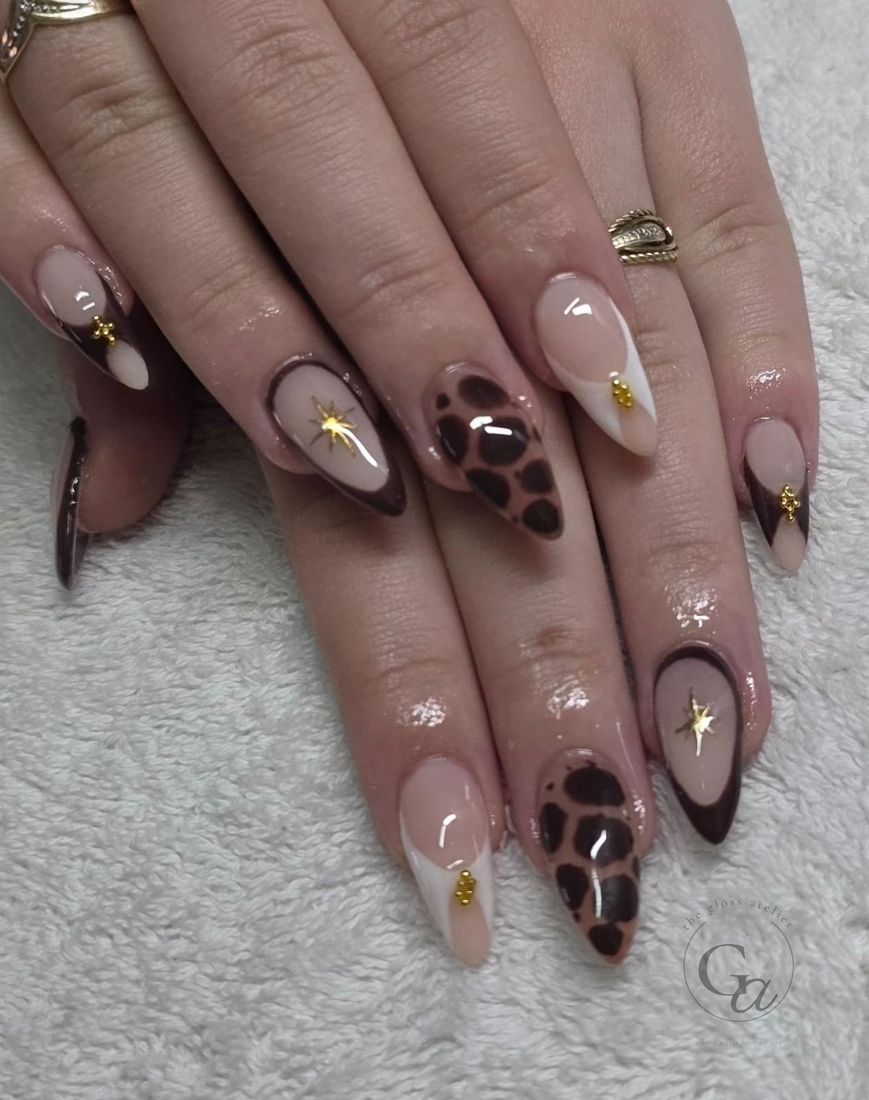 Chocolate-brown and cream almond nails with leopard print, gold stars and gold beads.