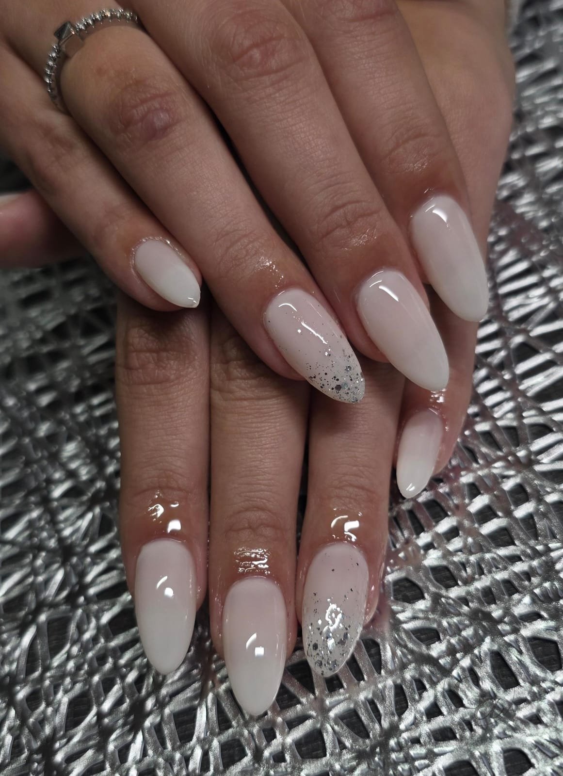 Milky white almond nails with silver glitter ombré accents.