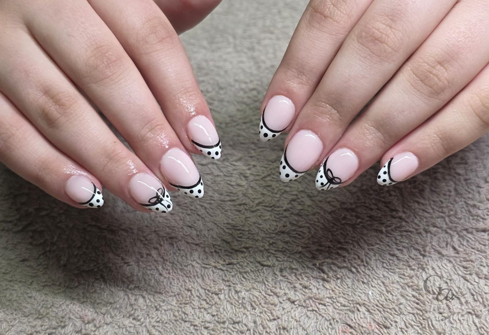 Nude almond nails with white polka-dot French tips and hand-painted black bows.