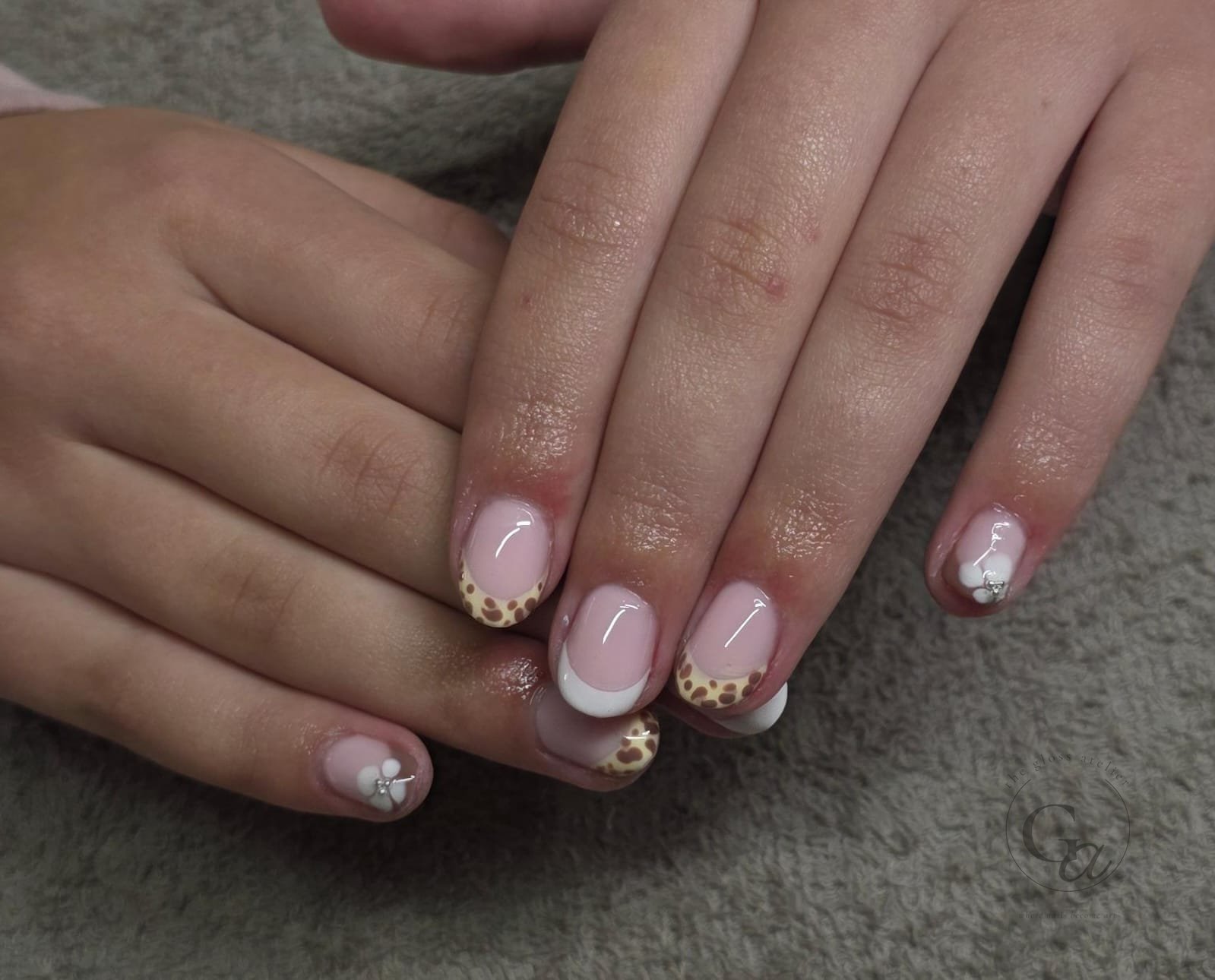 Short nails with leopard-print and white French tips and sculpted white flowers with crystals.