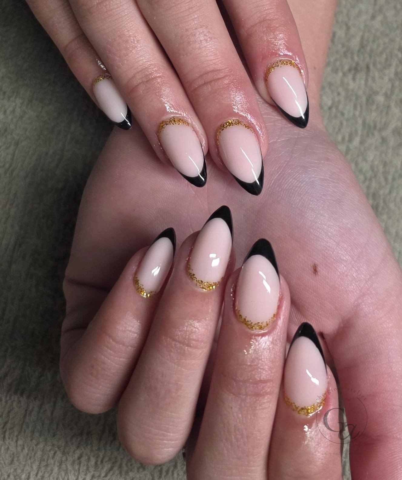 Nude almond nails with black French tips and gold glitter cuticle lines.