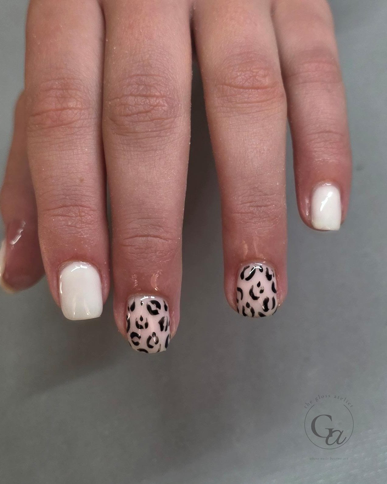 Short natural nails in cream with black leopard-print accent nails.