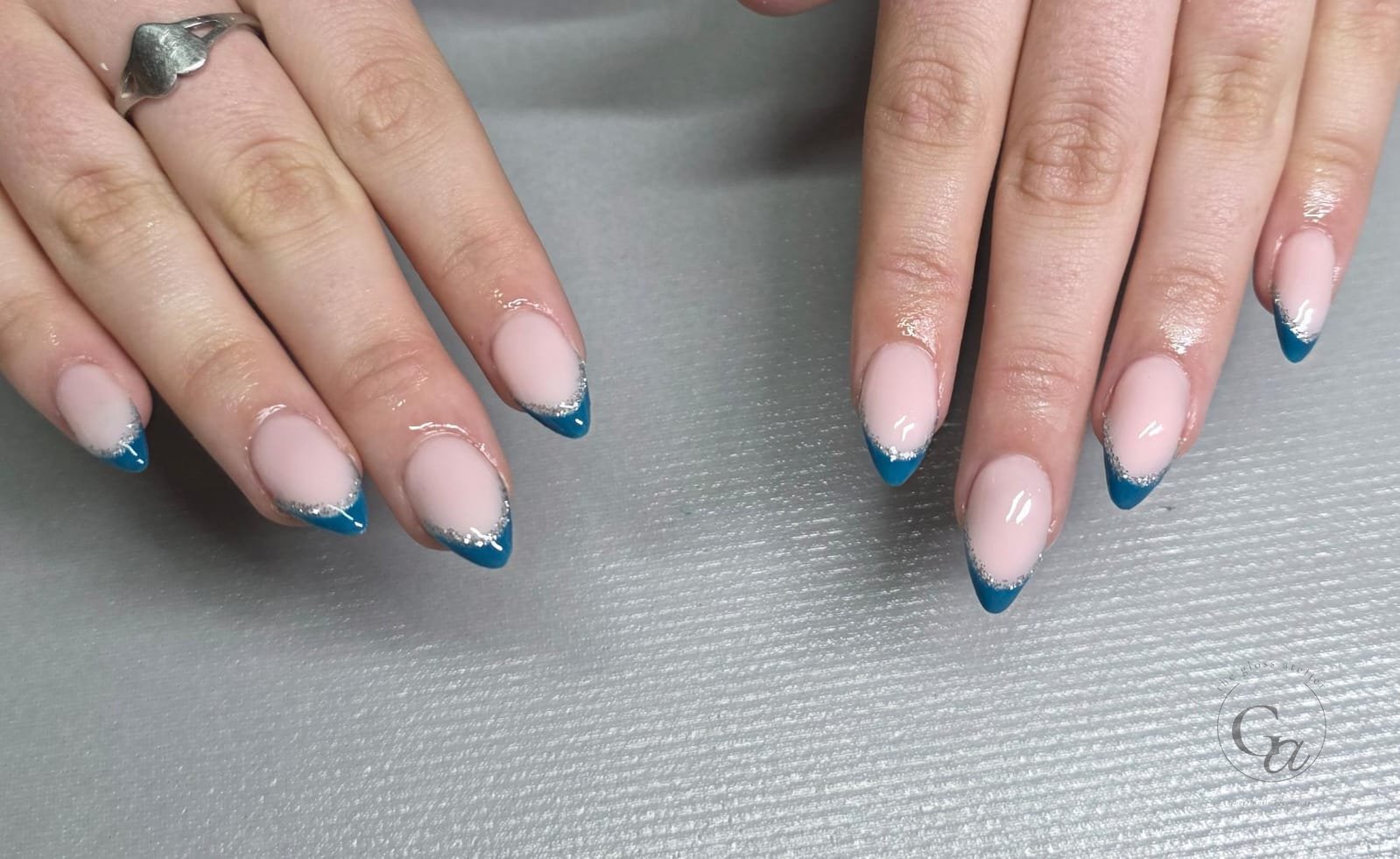 Teal French tips edged with silver glitter on almond nails.