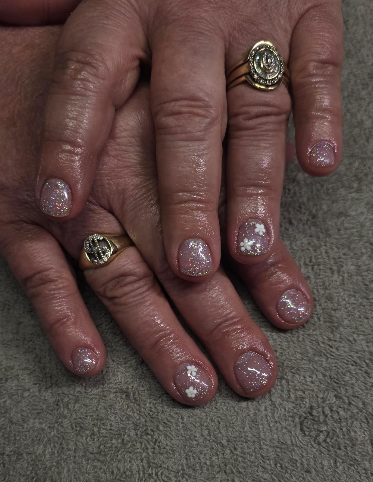 Short nails in iridescent glitter with sculpted white flowers.